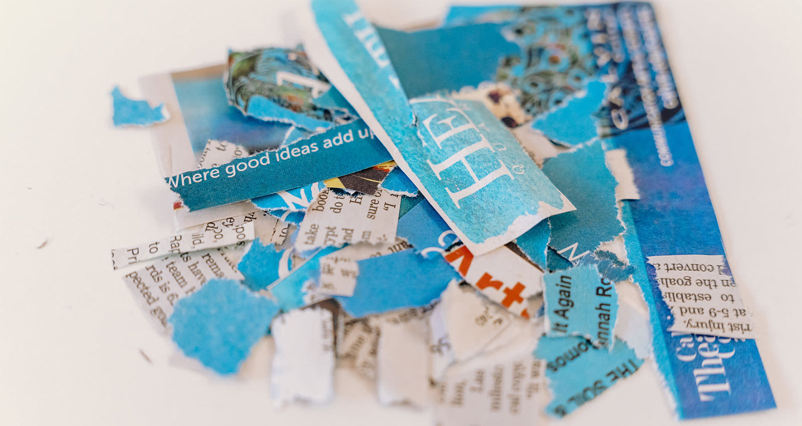 Small bits of various blue-colored newspaper are gently piled on a clean studio table.